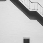 Black and white photo of a modern building's exterior staircase with strong shadows.